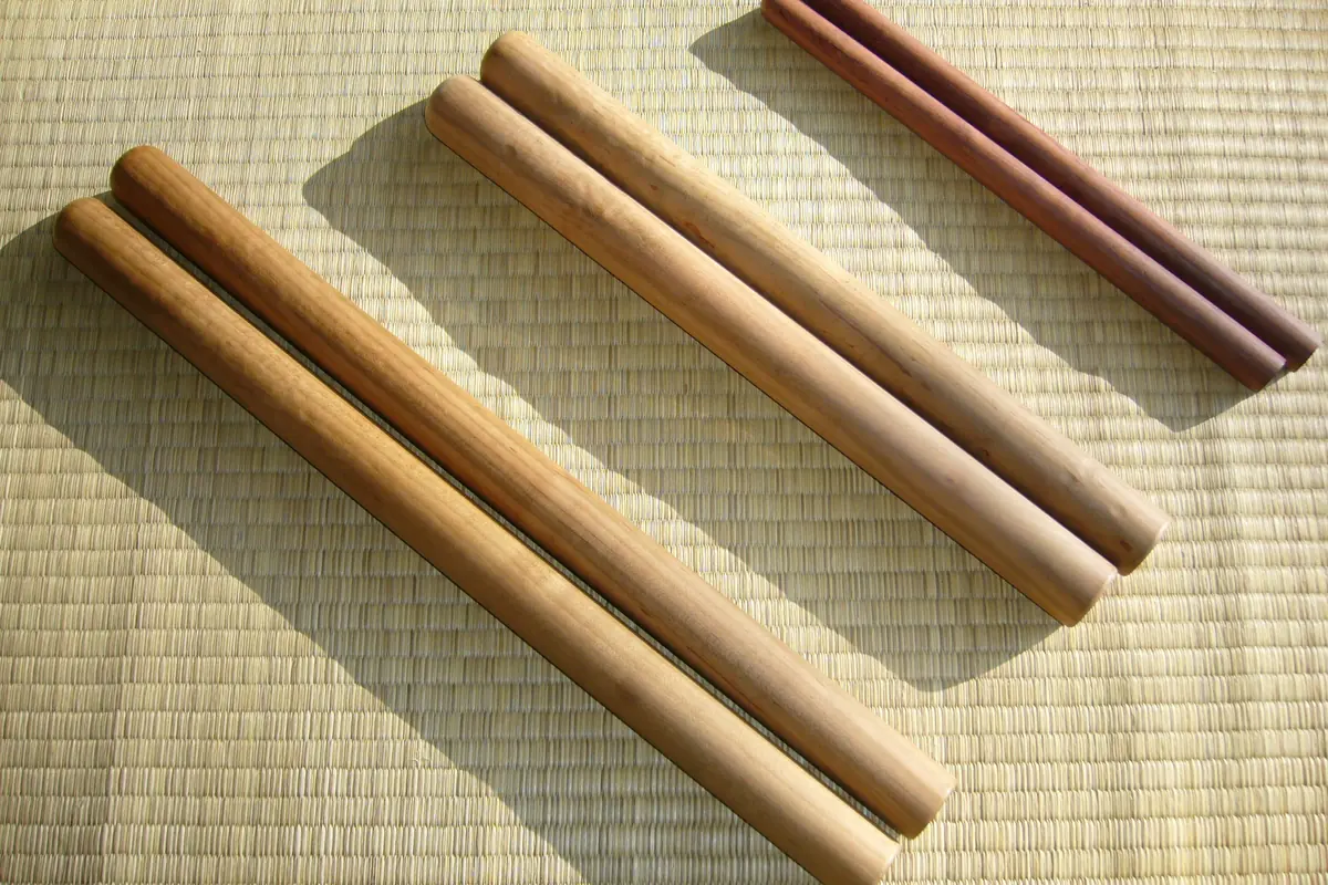 Tři páry dřevěných paliček taiko různé tloušťky leží na tatami